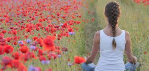Eine Frau beim Meditieren auf ein Feld mit blühendem Klatschmohn. (c) Pixabay.com