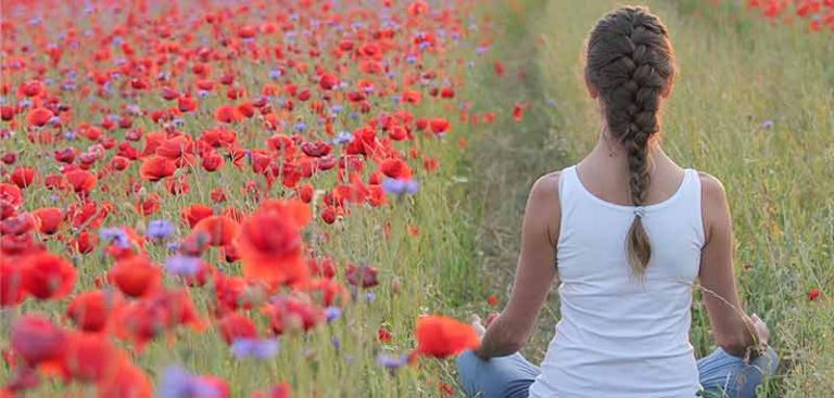 Eine Frau beim Meditieren auf ein Feld mit blühendem Klatschmohn. (c) Pixabay.com