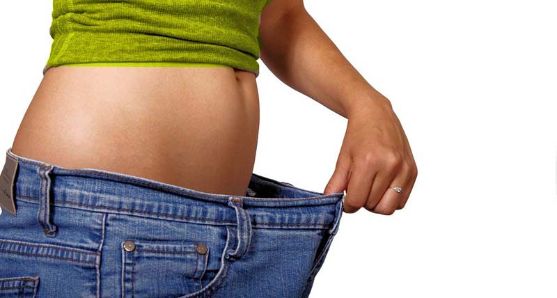 Eine Frau, die eine viel zu weite Hose von ihrem Bauch weghält, Stichwort Übergewicht.
(c) Pixabay.com