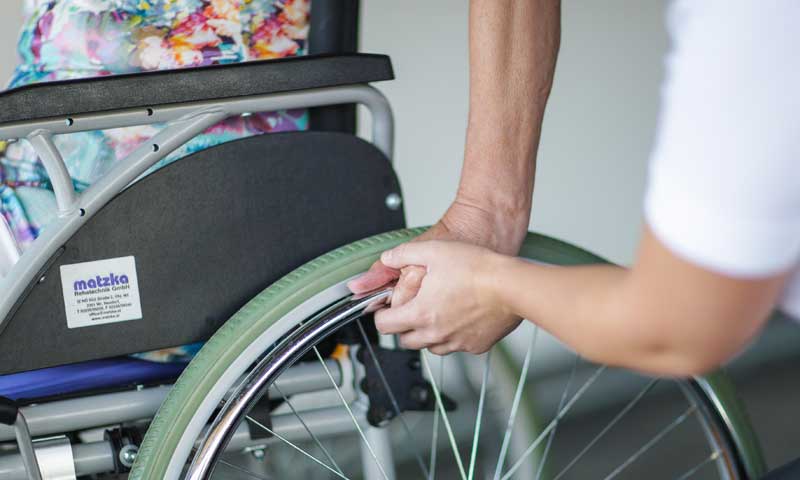 Die Hand einer Frau auf dem Rad ihres Rollstuhls sowie die einer Ergotherapeutin, die ihr dabei hilft. 
(c) Ergotherapie Austria/ Schultz & Schultz