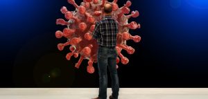 Post-Covid-Syndrom – mögliche Spätfolgen nach einer Infektion Ein Mann steht mit verschränkten Händen vor einem Corona-Virus. (c) Pixabay.com