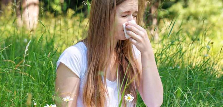 Eine junge Frau in einer blühenden Wiese, die sich die Nase putzt. (c) Freepik.com