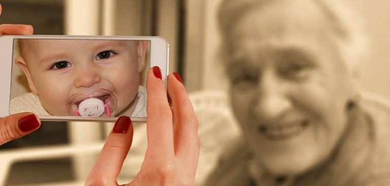 Die Hände einer Frau, die ein Smartphone mit einem Baby am Screen hält, dahinter eine lachende alte Frau. (c) Pixabay.com