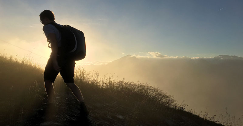 Ein Wanderer mit Rucksack bei aufgehender Sonne in den Bergen.
(c) Pixabay.com