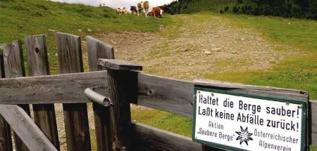 Eine Alm mit Kühen im Hintergrund, davor auf einem Zaun ein Schild mit: Haltet die Berge sauber. Laßt keinen Müll zurück." (c) Alpenverein/ B. Reitler