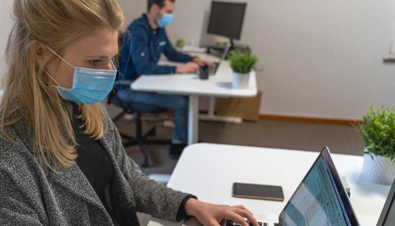 Eine Frau und im Hintergrund ein Mann mit Gesichtsmasken an Schreibtischen beim Arbeiten mit ihren Laptops.
(c) Pixabay.com