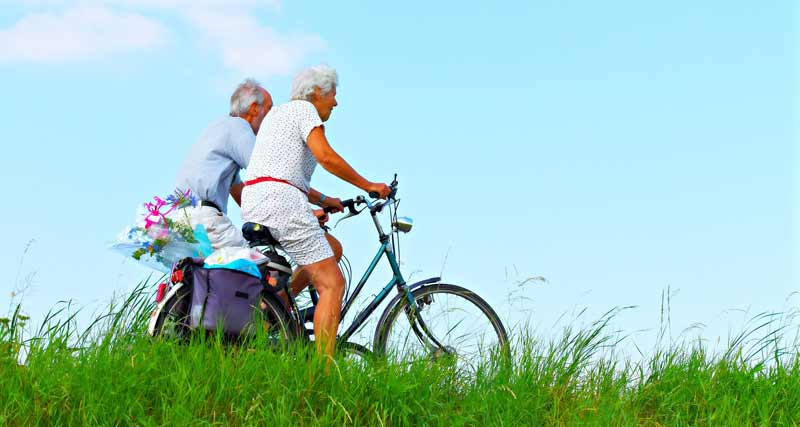 Ein älteres Ehepaar beim Radfahren neben einer Wiese.
(c) Pixabay.com