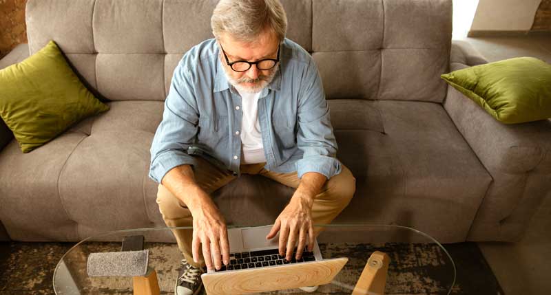 Ein älterer Mann mit Brille sitzt auf der Couch und tippt in seinen Laptop.
(c) AdobeStock