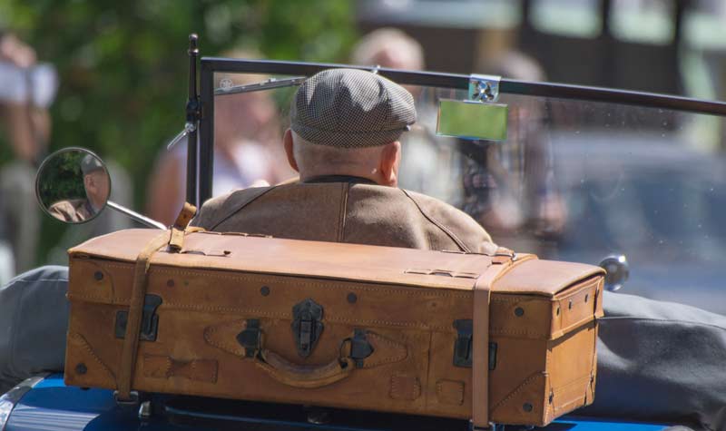 Ein alter Mann in einem Oldtimer-Cabrio, auf dem hinten ein Koffer moniert ist, Stichwort sicher durch den Sommer.
(c) Pixabay.com