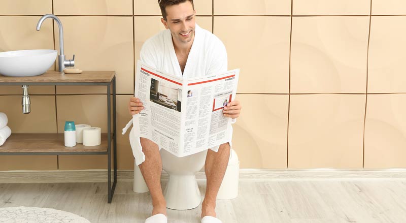 Ein Mann sitzt in den eigenen vier Wänden auf dem WC und liest Zeitung.
(c) AdobeStock