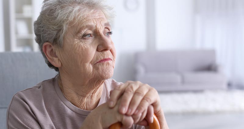 Das Gesicht einer alten Frau, die ihre Hände auf einen Gehstock stützt, Stichwort Einsamkeit.
(c) AdobeStock