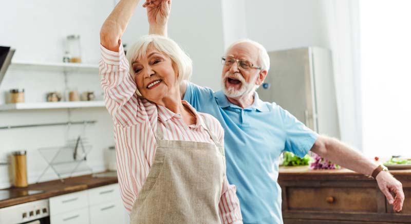 Ein älteres Ehepaar, das in der Küche beschwingt tanzt.
(c) AdobeStock