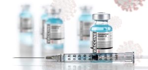 Corona: Geimpft oder infiziert – letztlich führt kein Weg daran vorbei Eine Spritze, dahinter Corona-Impfstoff. (c) AdobeStock