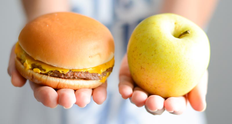 Die Hände einer Frau, die in einer Hand einen Burger und in der anderen einen Apfel hält.
(c) AdobeStock