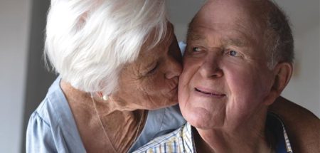 Das Gesicht eines alten Mannes, der von seiner Frau einen Kuss auf die Wange bekommt. (c) AdobeStock