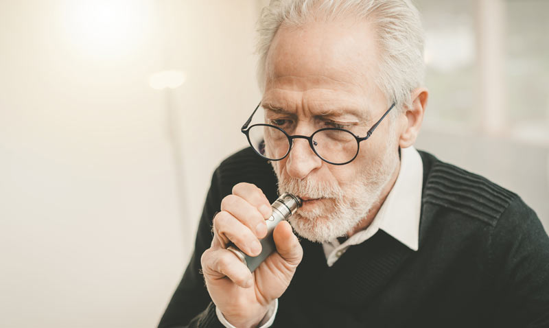 Ein alter Mann mit Brille und Bart zieht an einer E-Zigarette.
(c) AdobeStock