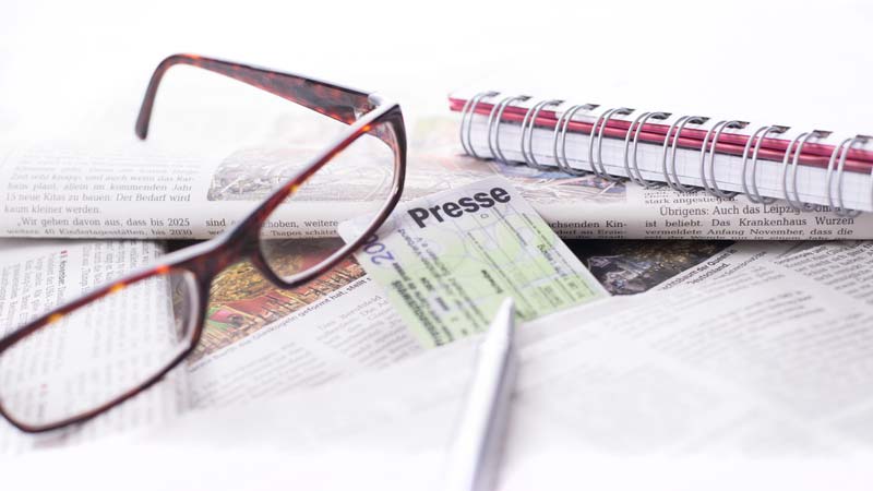 Eine Brille und ein Presseausweis auf diversen Zeitungen, Stichwort Impfskeptiker.
(c) AdobeStock