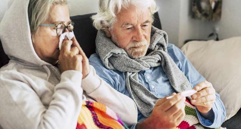 Ein älteres Paar, die Frau putzt sich die Nase, der Mann schaut auf einen Fieberthermometer, Stichwort Winter und influenza.
(c) AdobeStock
