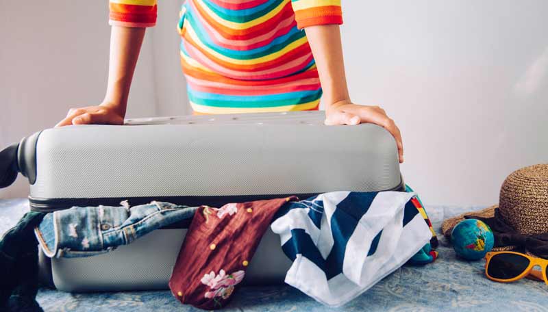 Reisen in Zeiten der Covid-Pandemie: hier finden Reisenden Tipps 1 Die Hände einer Frau, die einen überfüllten Reisekoffer zudrückt.
(c) AdobeStock