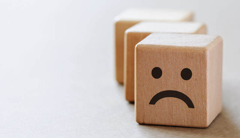Ein Holzwürfel mit einem traurigen Smiley, Stichwort depressiv.
(c) AdobeStock