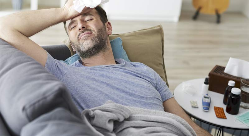 Ein kranker Mann auf der Couch, der sich die Hand auf die Stirn hält, Stichwort Doppelinfektion.
(c) AdobeStock