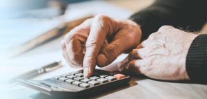 Die Hände einer alten Person, die einen Taschenrechner bedient. (c) AdobeStock