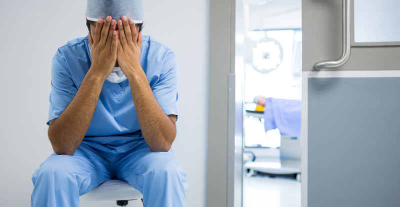 Ein Krankenpfleger, der auf einem Sessel sitzend die Hände vor sein Gesicht hält, Stichwort Belastung aufgrund der Pandemie.
(c) AdobeStock