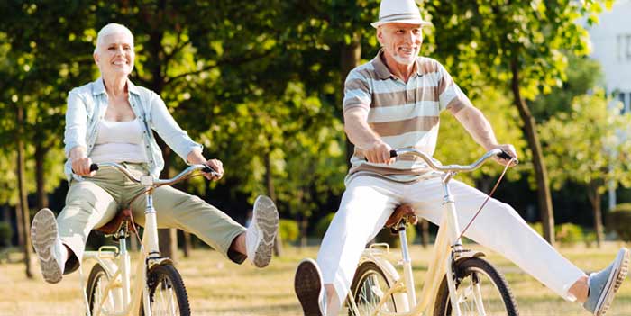 Ein älterer Mann mit Hut und eine ältere Frau auf einem Fahrrad; beide strecken die Füße von sich.
(c) AdobeStock