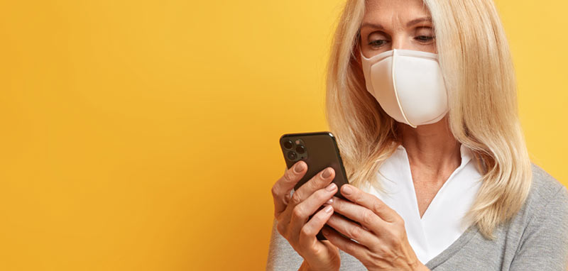 Eine Frau mit FFP2-Maske schaut auf ihr Smartphone. (c) AdobeStock