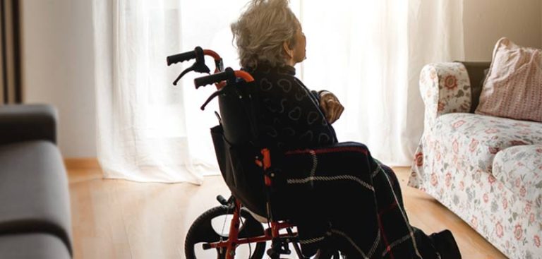 Eine alte Frau in einem Rollstuhl alleine in einem Zimmer. (c) AdobeStock