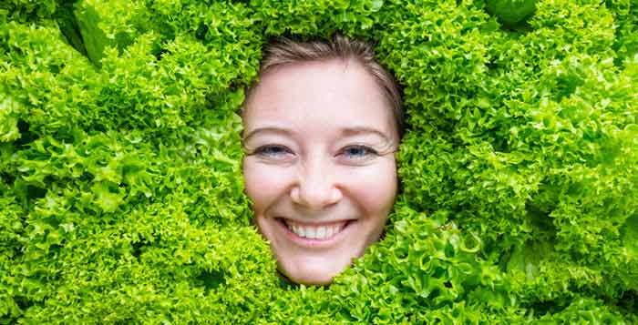 Das Gesicht einer Frau, die durch grünen Salat schaut.
(c) AdobeStock