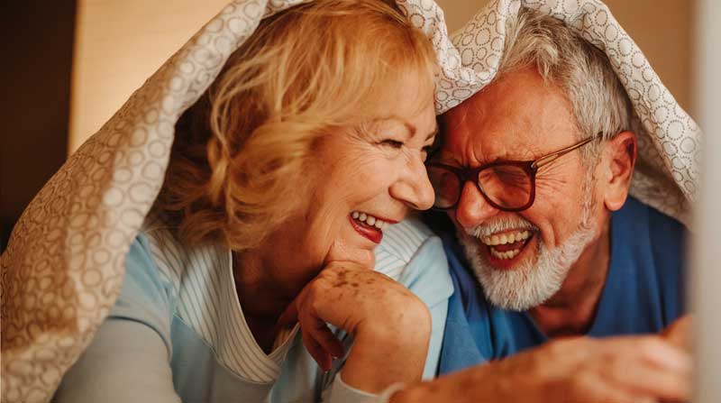 Ein älteres Paar lacht gemeinsam unter der Decke.
(c) AdobeStock