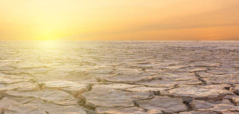 Ausgetrocknete Landschaft, am Horizont die heiße Sonne. (c) AdobeStock