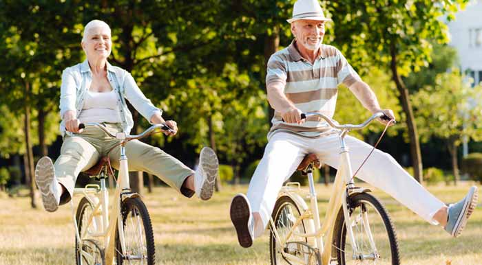 Ein älteres Paar auf Fahrrädern; beide strecken amüsiert die Beine nach vor, Stichwort AlterNEUdenken.
(c) AdobeStock