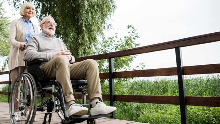 Eine ältere Frau schiebt einen Rollstuhl, in dem ein älterer Mann mit weißem Bart sitzt.
(c) AdobeStock