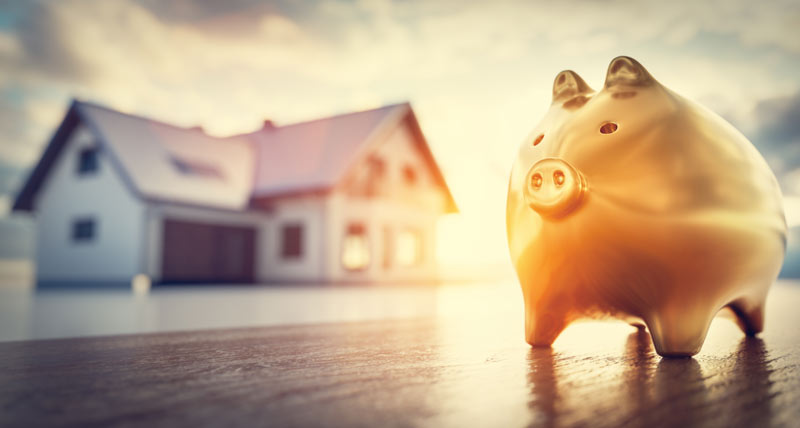 Ein Sparschwein im Vordergrund, dahinter ein Haus, Stichwort Geld für die Finanzierung.
(c) AdobeStock