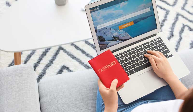 Eine Frau mit Laptop und Reisepass auf der Couch bei der Buchung eines Fluges über ein Online-Portal.
(c) AdobeStock
