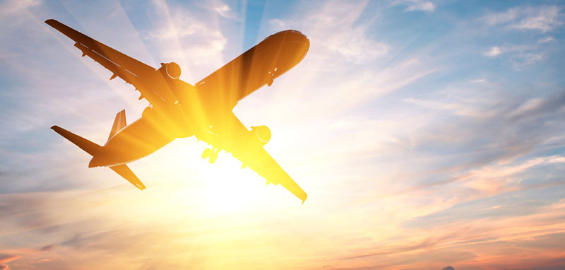 Ein Flugzeug in der Luft vor der untergehenden Sonne. (c) AdobeStock