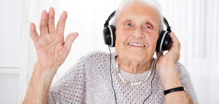 Eine alte Frau mit Kopfhörern freut sich an der Musik, die sie hört. (c) AdobeStock