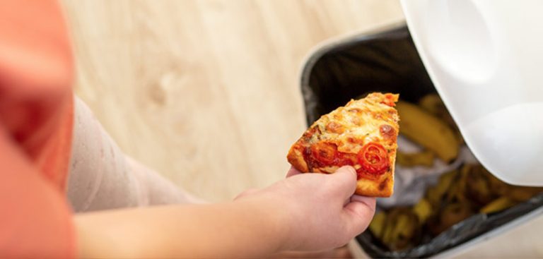 Die Hand einer Frau, die ein Stück Pizza in einen Mülleimer wirft. (c) AdobeStock