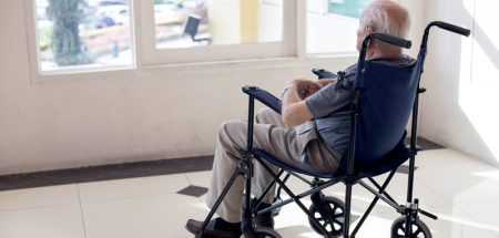 Ein alter Mann in einem Rollstuhl sitzt vor einem Fenster und schaut hinaus. (c) AdobeStock