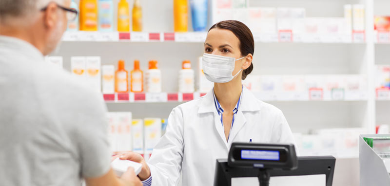 Ein Mann, der von einer Apothekerin mit Maske ein Medikament bekommt. (c) AdobeStock