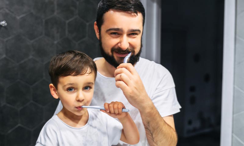 Ein Mann und ein Kind, die sich die Zähne putzen, Stichwort Zahngesundheit.
(c) AdobeStock