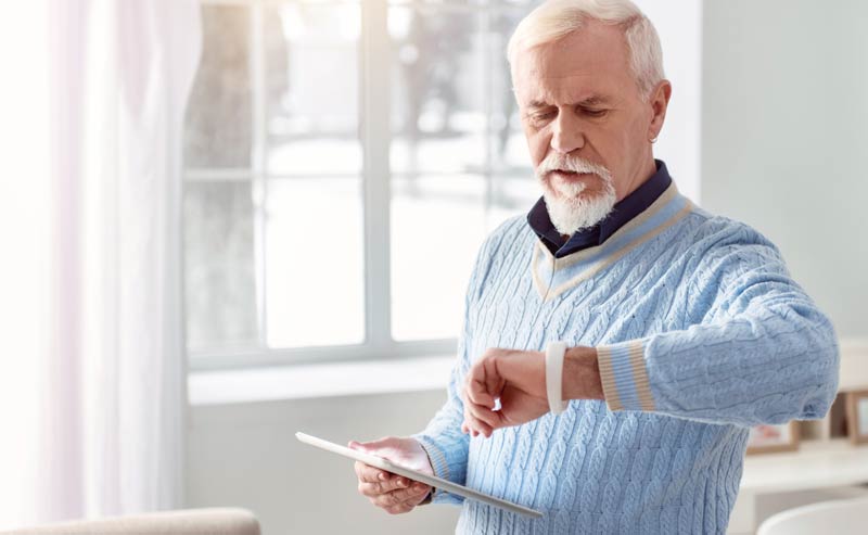 Ein älterer Mann mit Tablet in der Hand schaut auf seine Smartwatch, Stichwort Lebensqualität im Alter.
(c) AdobeStock
