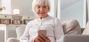 Eine alte Frau sitzt auf einer Couch mit einem Smartphone in der Hand. (c) AdobeStock