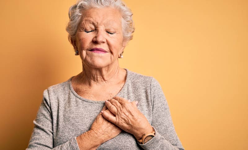 Eine ältere Frau mit geschlossenen Augen, die sich mit beiden Händen auf ihr Herz greift.
(c) AdobeStock