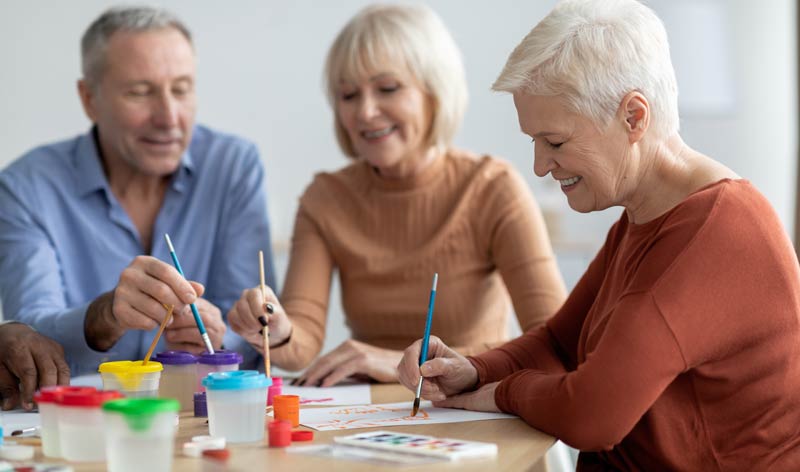 Zwei ältere Frauen und ein älterer Mann beim Zeichnen mit Wasserfarben, Stichwort aktiv im Alter.
(c) AdobeStock