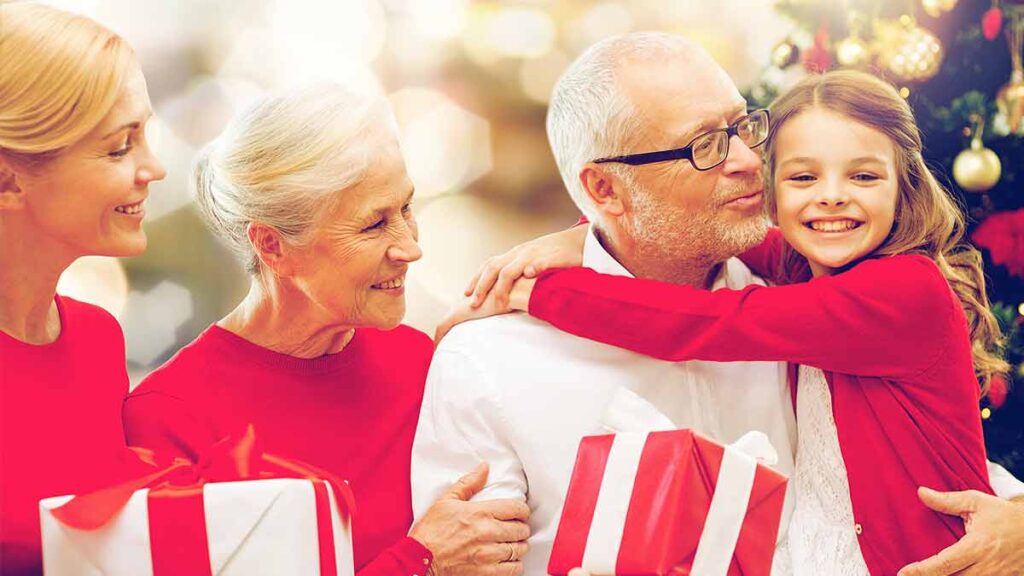 Familie mit Kind, Tochter und Großeltern mit Geschenken vor einem Weihnachtsbaum. (c) AdobeStock