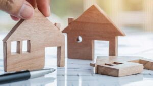 FMA: „Reden wir über Geld“ – Tipps zum Thema Haushaltsversicherung Die Hand eines Mannes, der einen Seitenteil eines Modells eines Hauses aufstellt. (c) AdobeStock