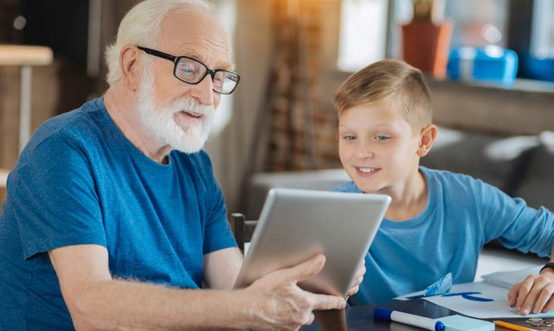 Ein älterer Mann mit Tablet neben einem Kind; beide schauen ins Tablet.
(c) AdobeStock